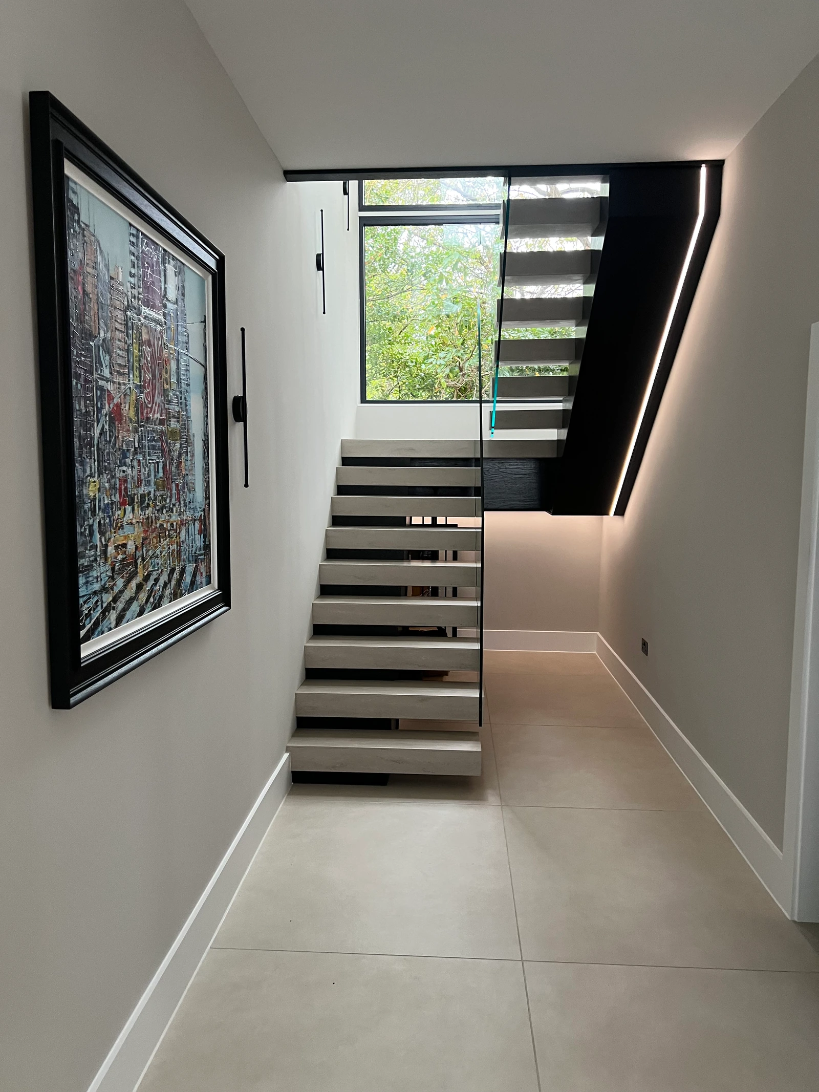 Finished staircase in the completed hallway, with black oak, pale treads and clear glass.
