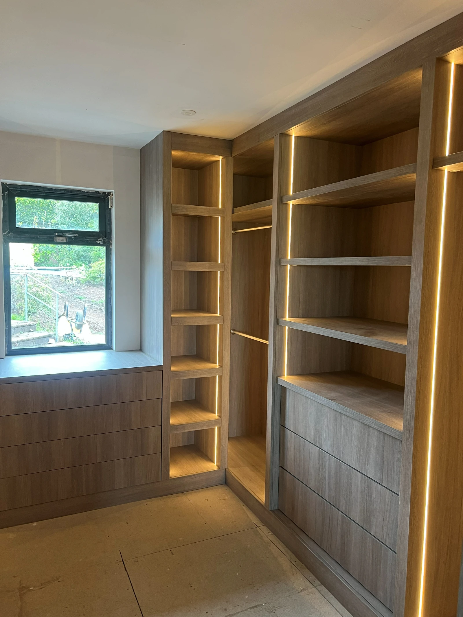 Installed oak dressing-room cabinetry wrapping from drawer storage into illuminated shelves and hanging space