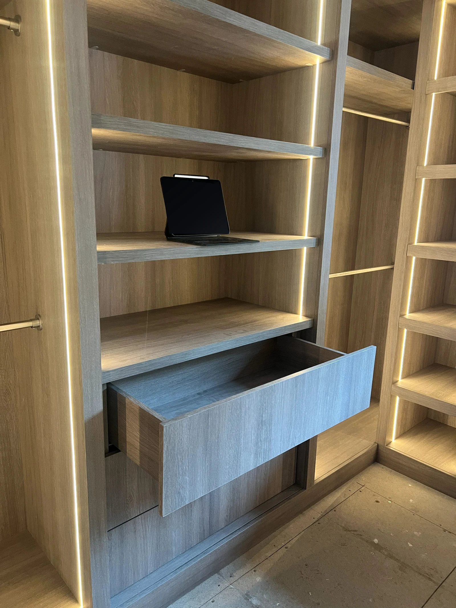 Installed oak cabinetry with one full-depth drawer open beside illuminated hanging and display storage