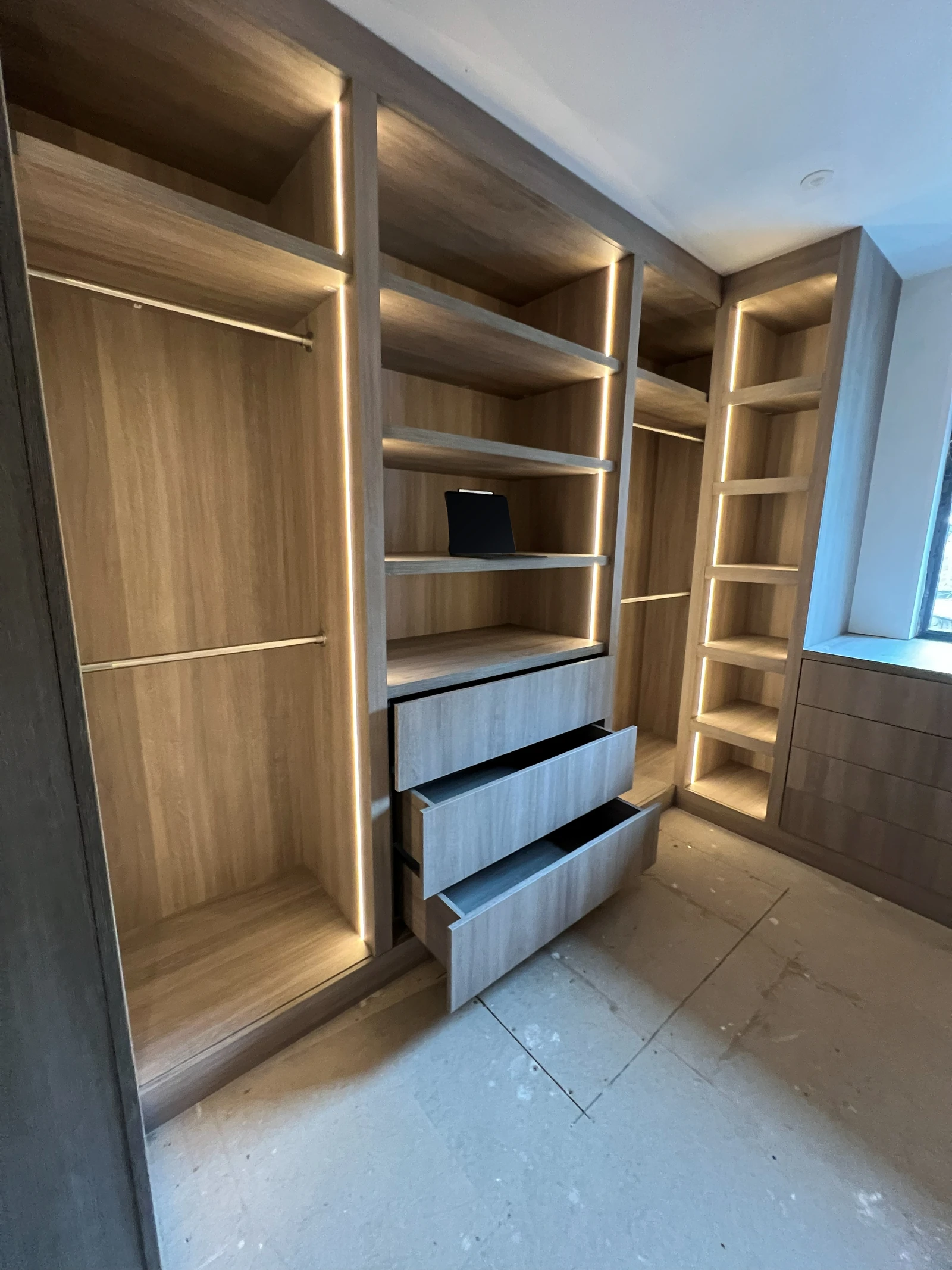 Wide view of the installed wraparound dressing-room joinery with drawers open and integrated lighting