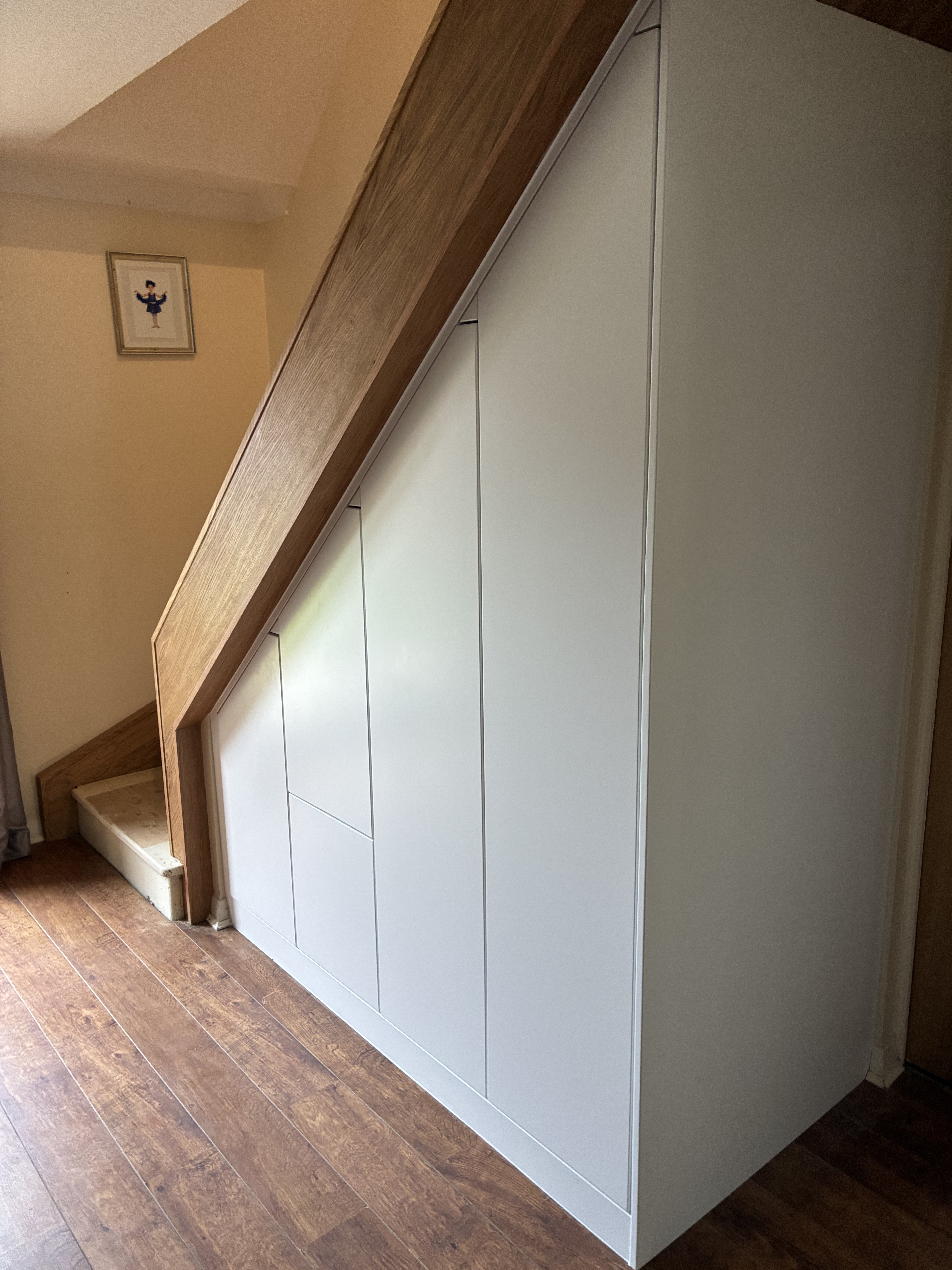 Client-supplied site photograph of the fitted white understair cabinet fronts, before stair glass installation.